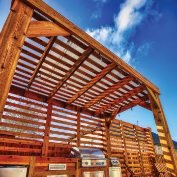 A cedar-stained wooden pergola with slatted privacy wall is covered with Skypoly Apollo Clear.