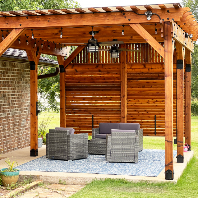 A cedar-stained pergola with a privacy wall sits above a concrete slab with outdoor furniture.