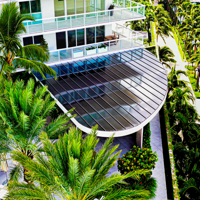 A large, curved top view entrance to a condo is covered with Skypoly Hercules Bronze and flanked on one side by palm trees.