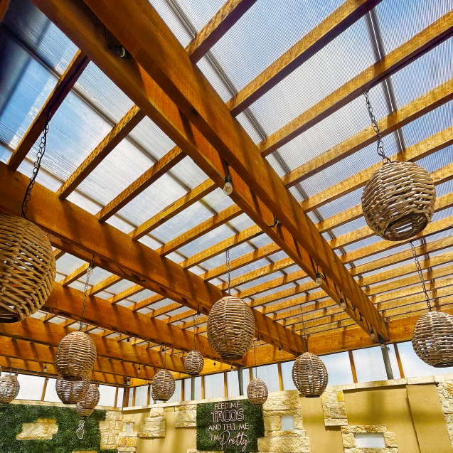 An outdoor eating area at a restaurant is covered by a pergola with Skypoly Hercules Bronze and circular wicker hanging lights.